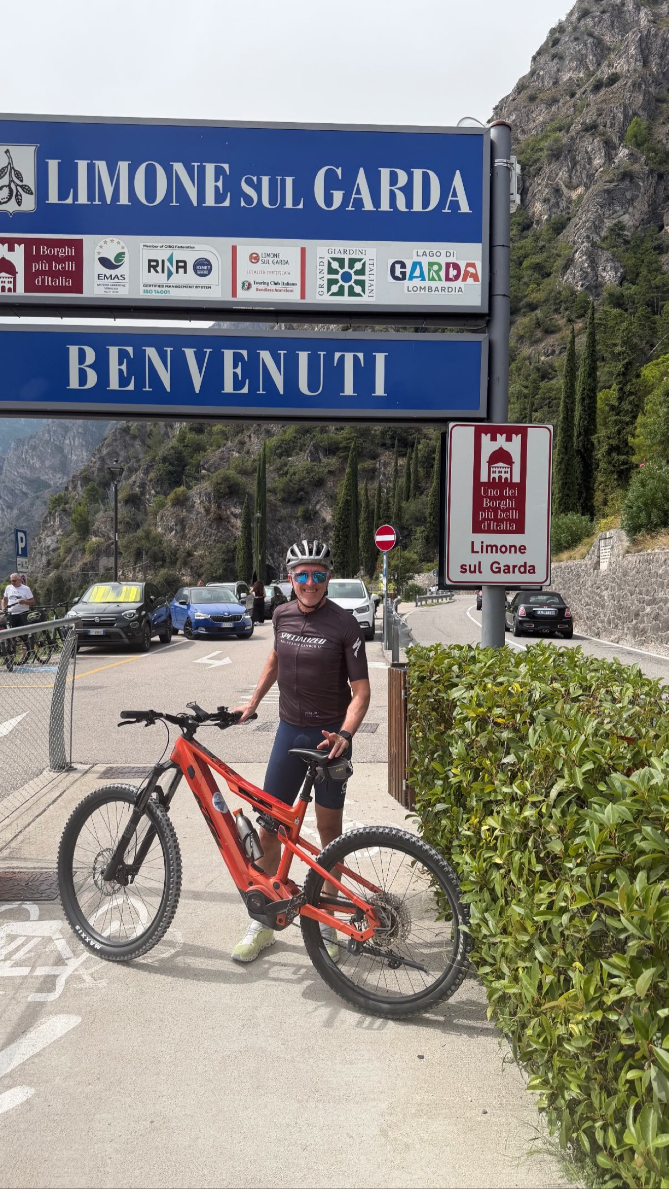 Cyclist with a red e-mountain bike beneath the Limone sul Garda welcome sign